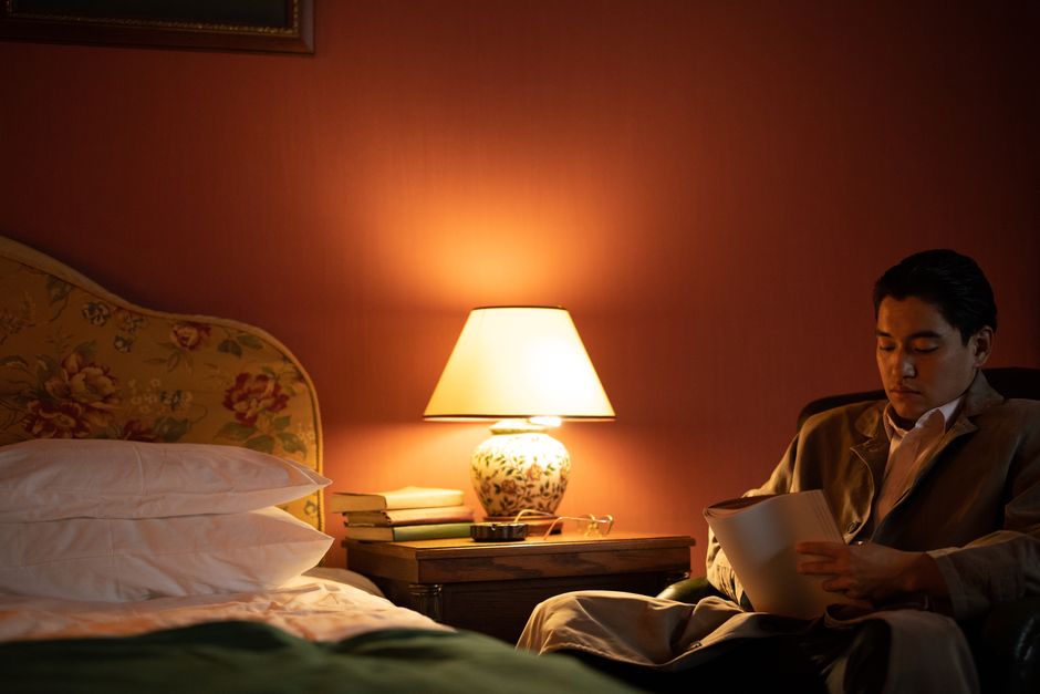 Homme assis dans une chambre chaleureuse, lisant un livre près d'une lampe douce, ambiance propice à la détente.