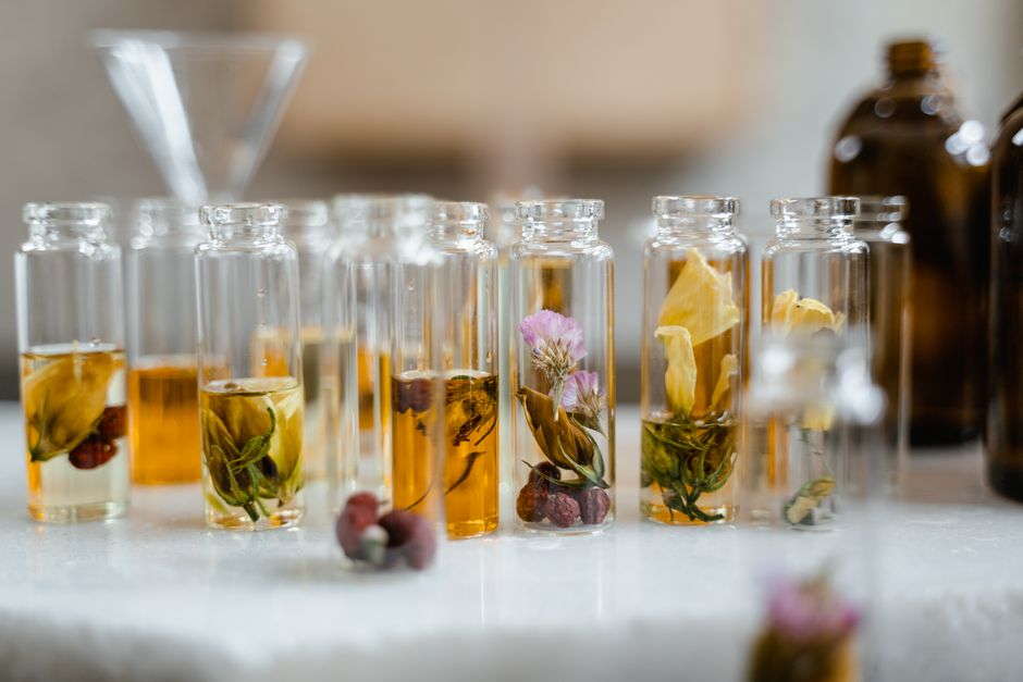 Flacons transparents contenant des huiles végétales et des fleurs, sur une table en marbre, pour un article sur les soins de