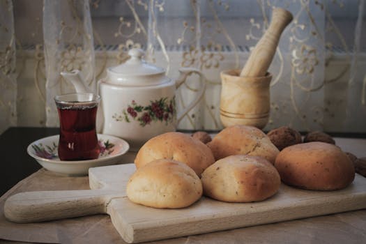 Pains maison frais sur une planche en bois, accompagnés d'une tasse de thé et d'ustensiles de cuisine, décor chaleureux.