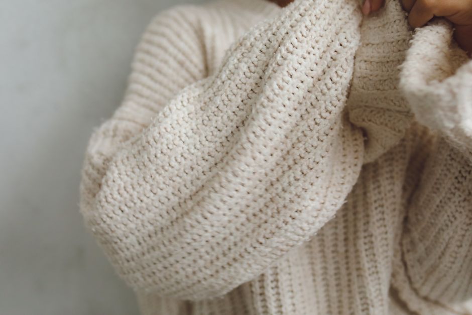 Personne portant un pull en tricot beige, se protégeant les mains du froid.