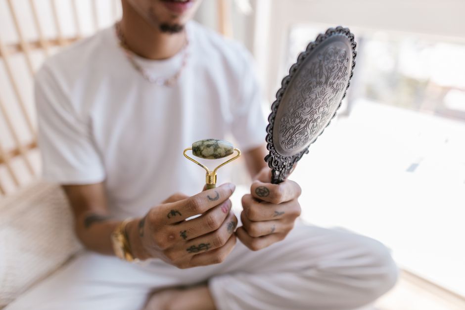 Homme tenant un rouleau de jade et un miroir, prêt à pratiquer l'auto-massage du visage à la maison.