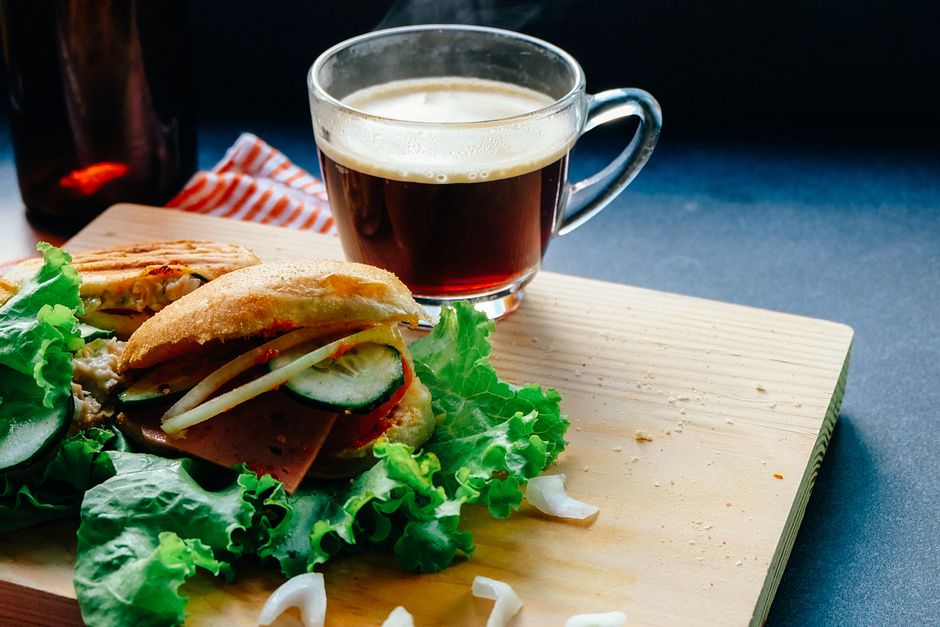 Sandwich garni de légumes sur une planche en bois, avec une tasse de café fumant à côté.