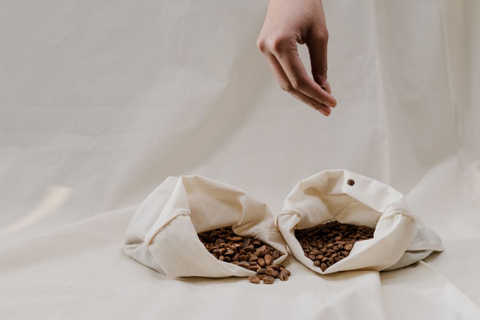 Main versant des grains dans des sacs en tissu sur un fond neutre, illustrant le zéro déchet.