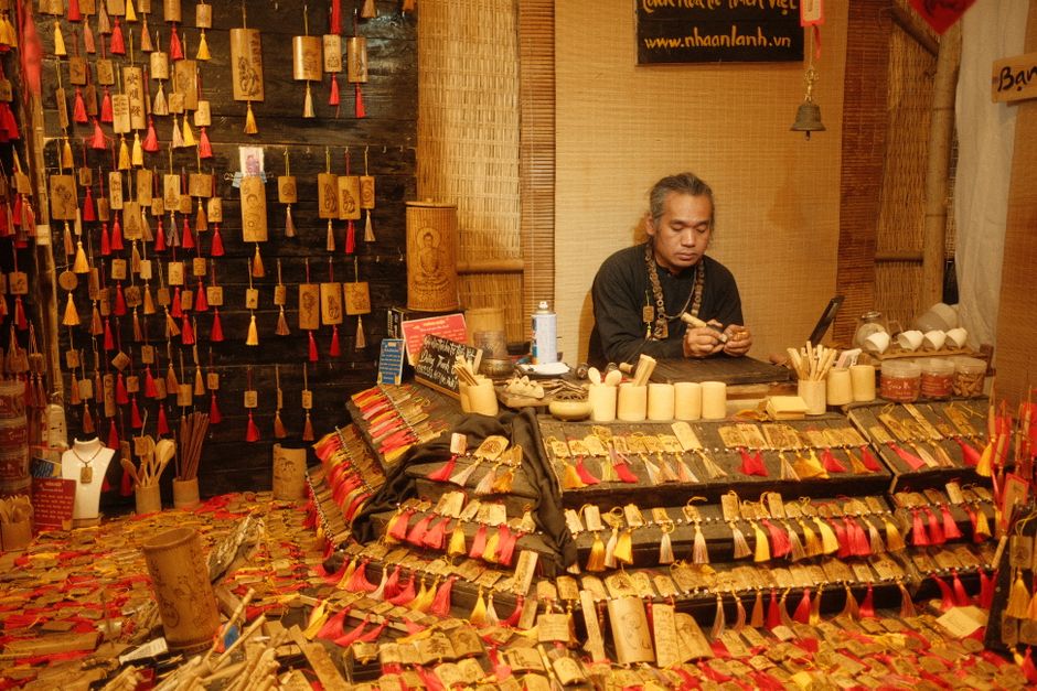 Artisan travaillant sur des objets en bois dans un marché, entouré de créations artisanales colorées.