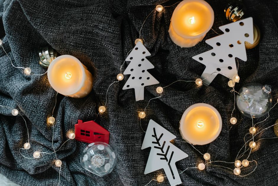 Décor cocooning avec bougies, guirlande lumineuse et décorations de Noël sur un plaid gris.