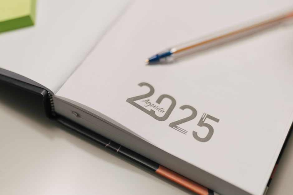 Agenda ouvert sur l'année 2025 avec un stylo à bille posé à côté, sur un bureau.