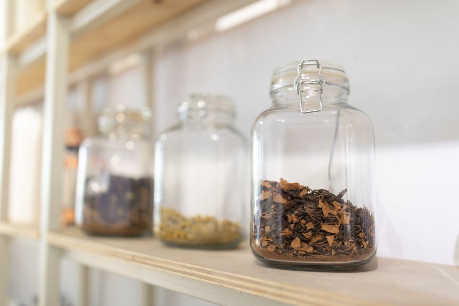 Bocaux en verre remplis de plantes séchées sur une étagère en bois, illustrant une approche zéro déchet.