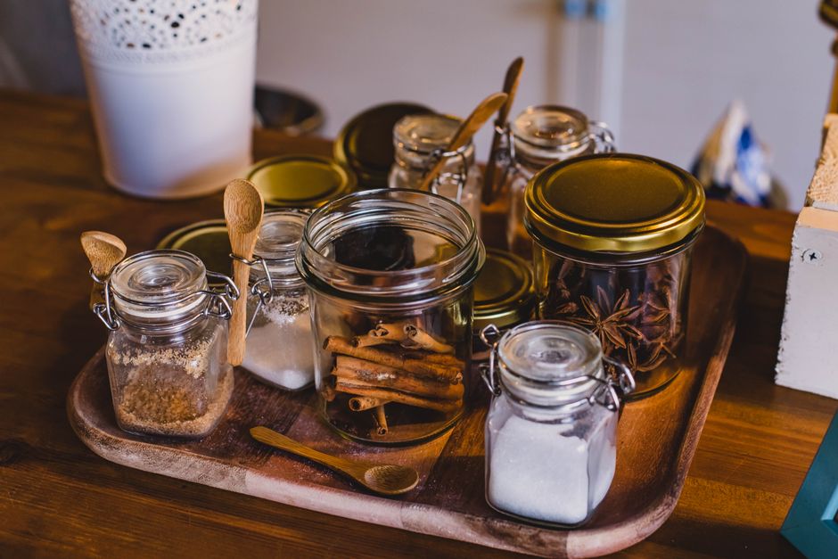 Bocaux en verre remplis d'épices et de sucre sur un plateau en bois, illustrant une approche zéro déchet.