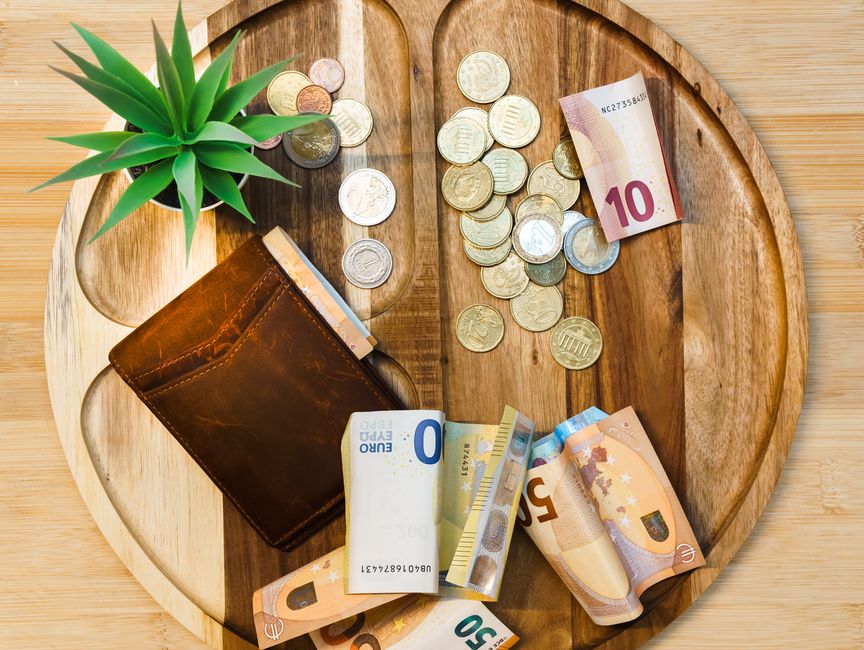 Plateau en bois avec un portefeuille, des pièces de monnaie et des billets en euros, symbolisant la gestion budgétaire.