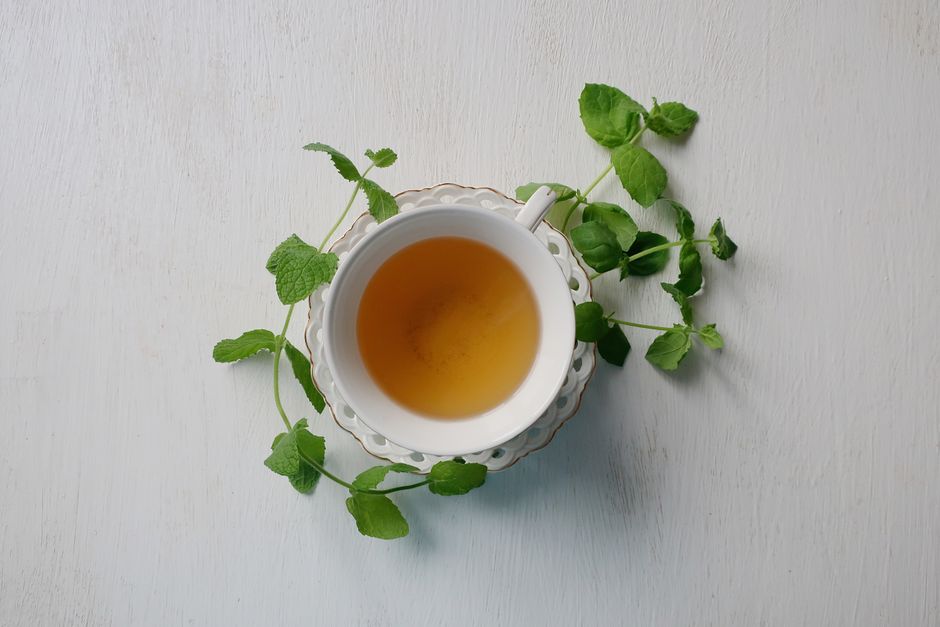 Tasse de thé infusé entourée de feuilles de menthe sur une soucoupe blanche.