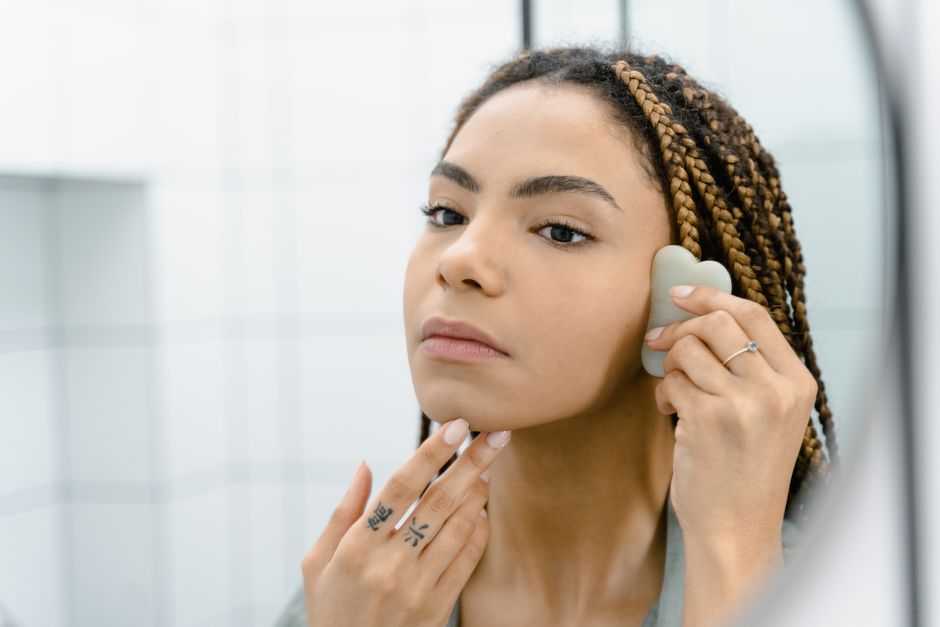 Femme utilisant un outil de massage facial devant un miroir dans une salle de bain.