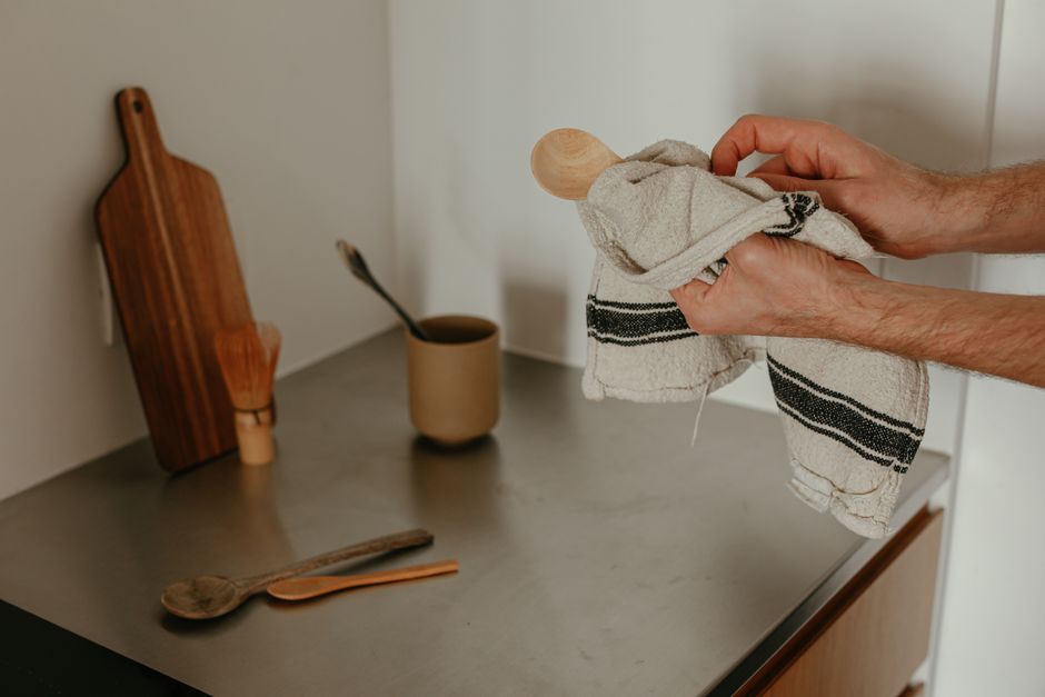 Personne essuyant une cuillère en bois avec un torchon réutilisable sur un plan de travail en métal.