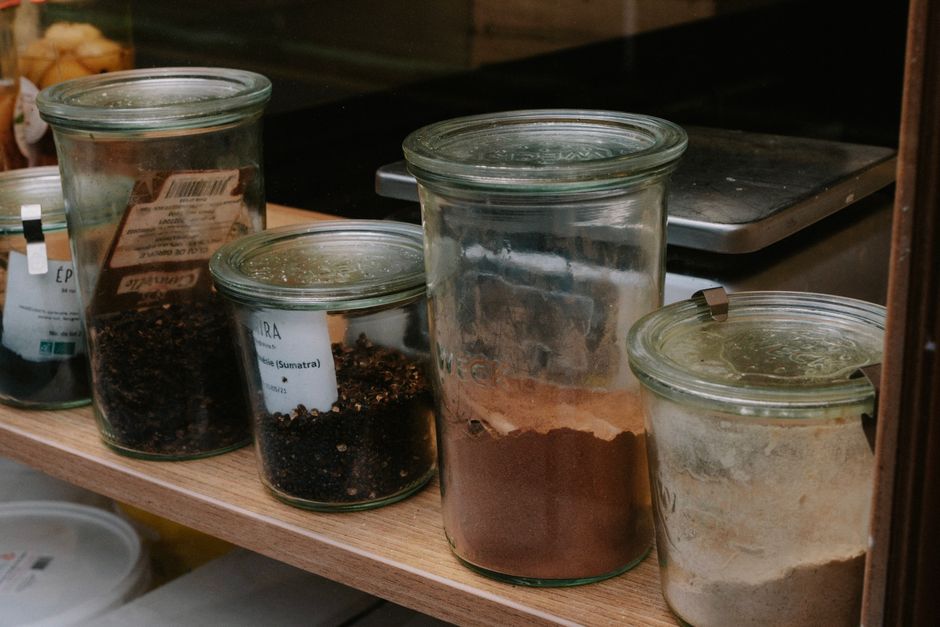 Bocaux en verre contenant des épices et des ingrédients en vrac sur une étagère en bois dans une cuisine.