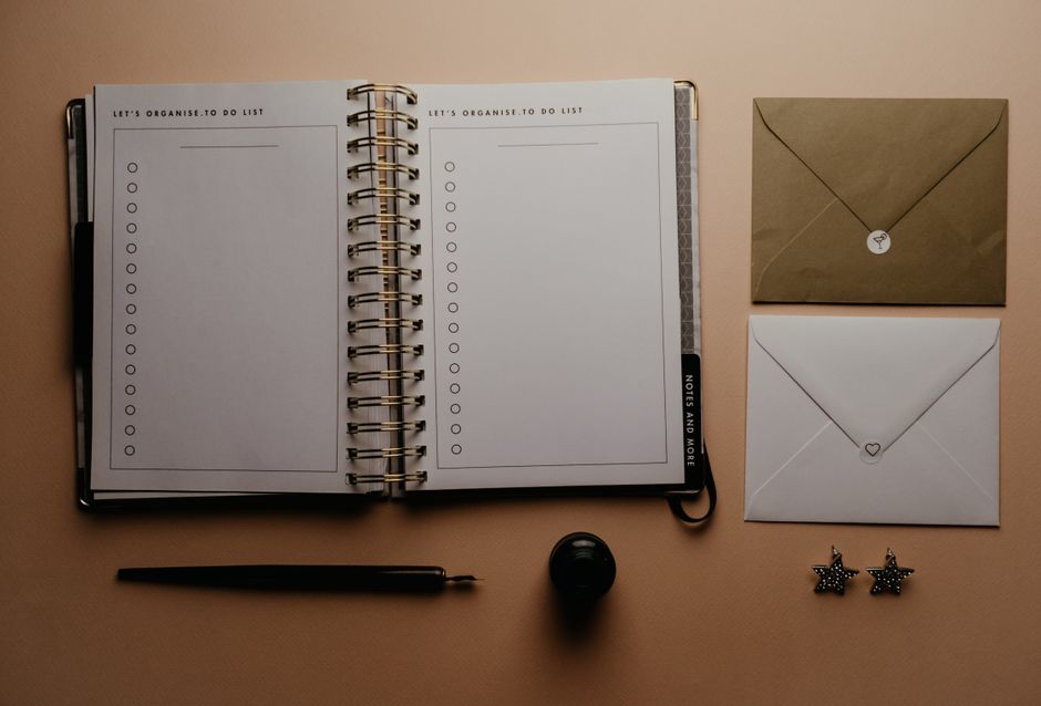 Carnet ouvert avec une liste de tâches vierge, stylos, enveloppes et boucles d'oreilles sur une surface beige.