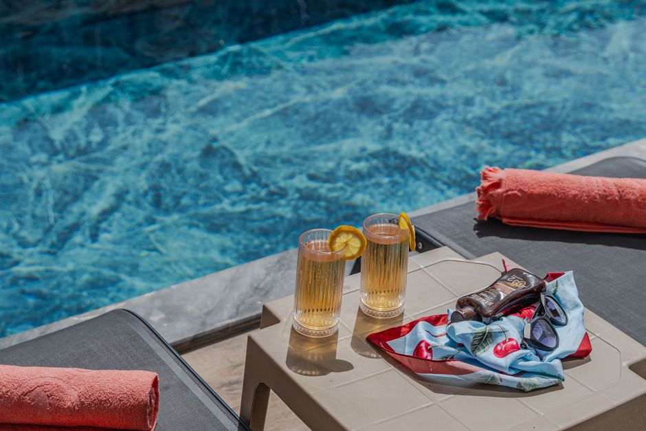 Deux verres de boisson avec des tranches de citron sur une table près d'une piscine, accompagnés d'une serviette et d'un foul