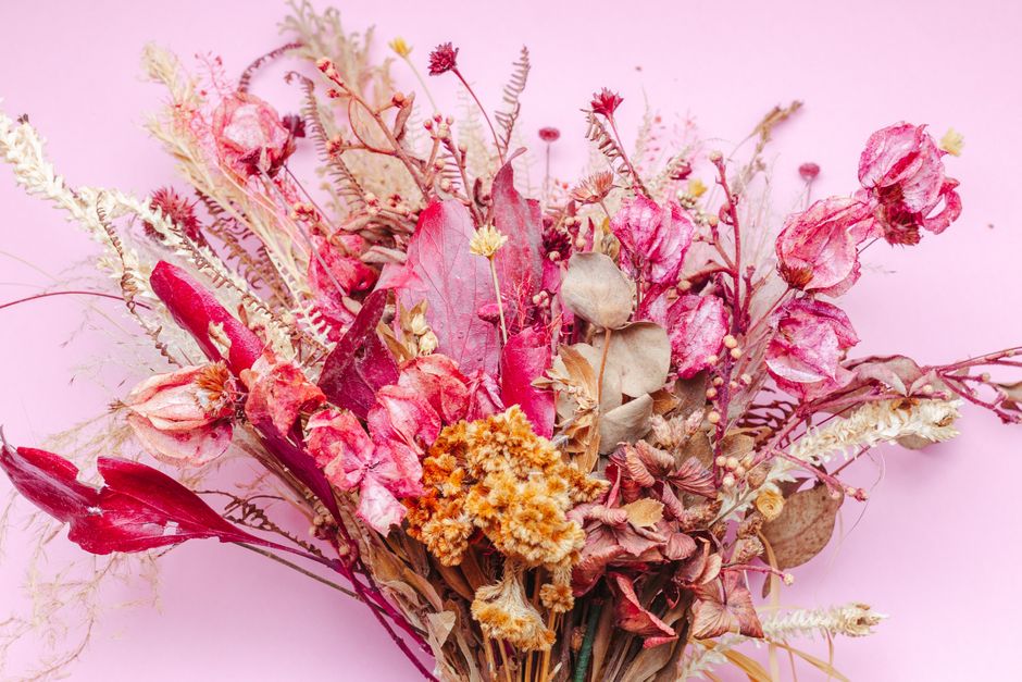 Bouquet de fleurs séchées aux teintes roses et dorées sur fond rose, parfait pour des idées de cadeaux originaux.