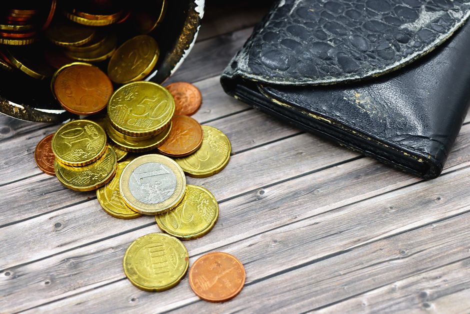 Porte-monnaie usé avec des pièces de monnaie éparpillées sur une surface en bois, illustrant les dépenses impulsives.