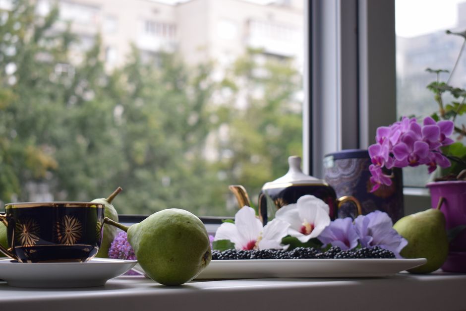 Tableau de fruits, fleurs et thé sur un rebord de fenêtre, créant une ambiance apaisante pour une routine matinale.