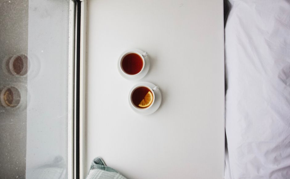 Deux tasses de thé posées sur une table près d'une fenêtre, avec un oreiller et une couverture en arrière-plan.