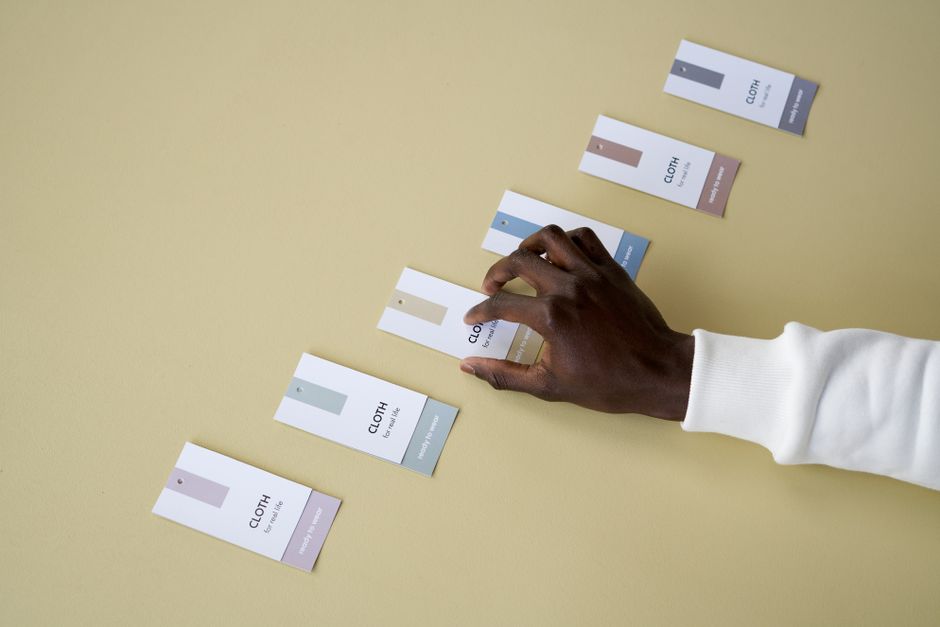 Main noire examinant des étiquettes de produits textiles sur une table beige, mettant en avant l'importance de lire les ingré