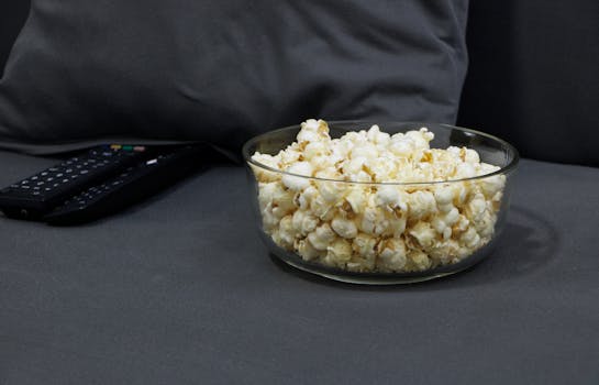 Bol de popcorn sur un canapé gris avec une télécommande à côté, prêt pour une soirée cinéma.