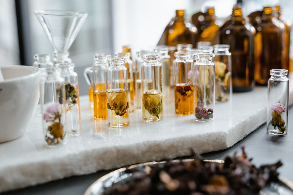 Flacons en verre contenant des huiles végétales et des fleurs, disposés sur une table en marbre.